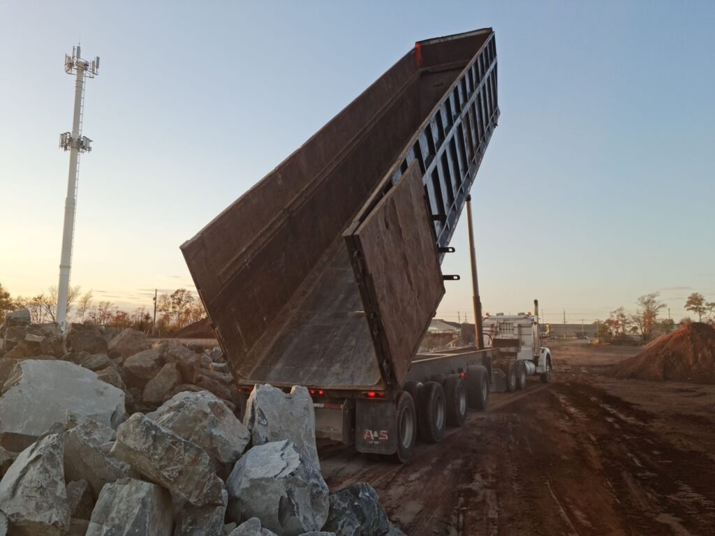 Camión de volteo descargando material pétreo en una obra al atardecer