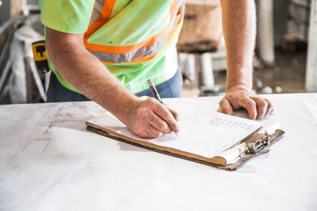 Supervisor de obra anotando en un portapapeles sobre planos de construcción