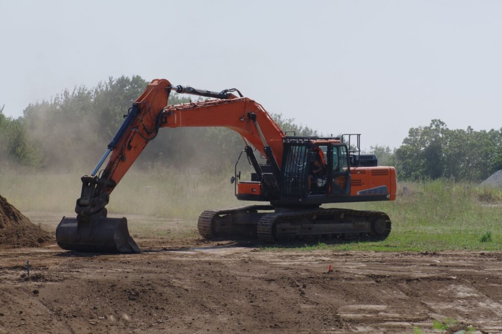 Excavadora hidráulica ejecutando un corte de terreno con polvo en la obra