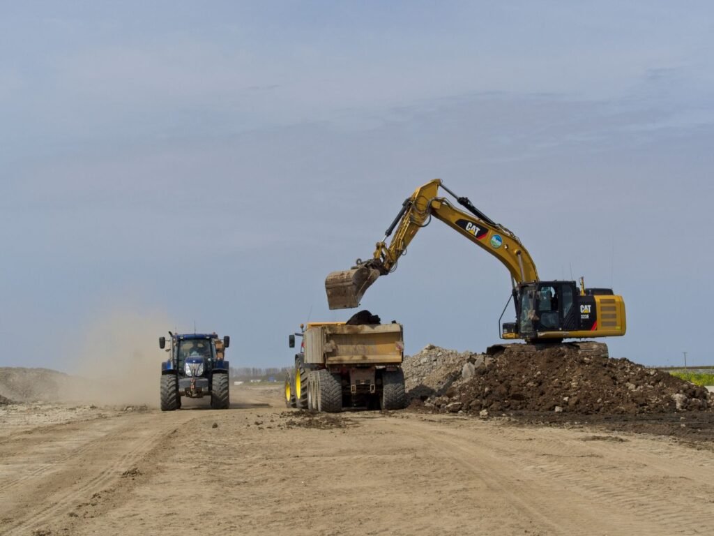 Excavadora cargando material en un camión de volteo en una obra con polvo
