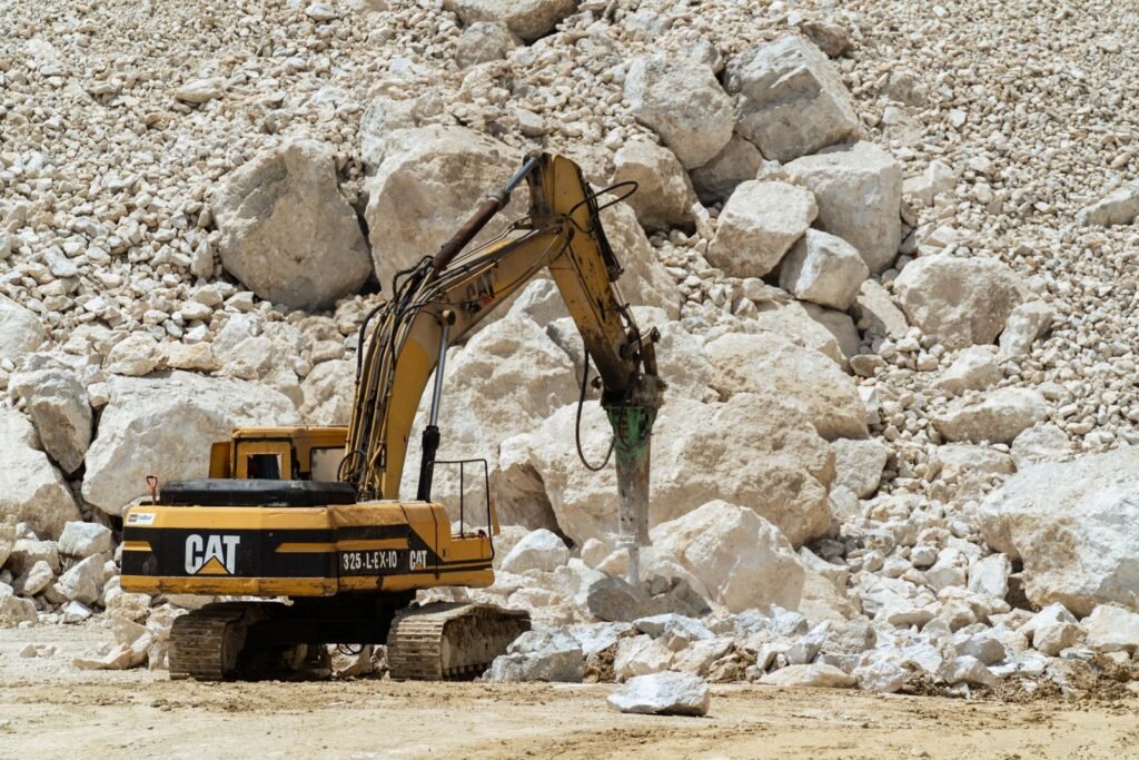 Excavadora con martillo hidráulico rompiendo roca en un banco de material