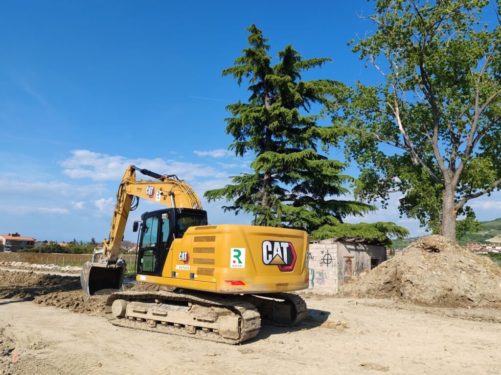 Excavadora de orugas Caterpillar amarilla en una obra con árboles al fondo