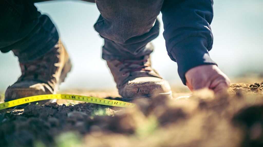 Manos midiendo el suelo con una cinta métrica a ras de terreno