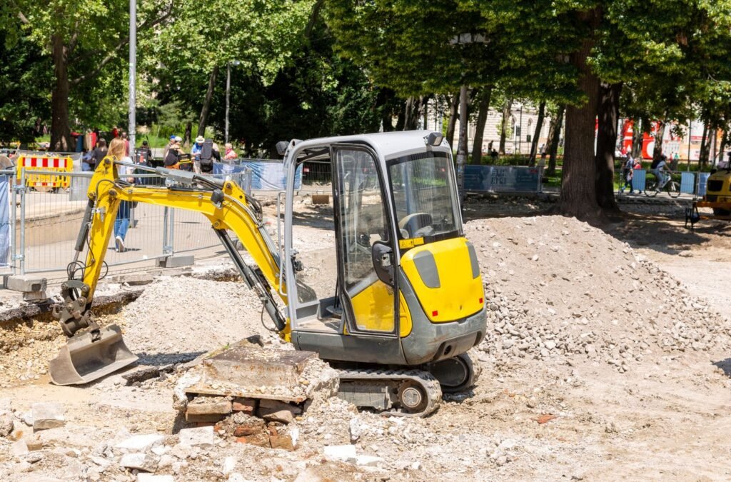 Mini excavadora trabajando en una banqueta con escombro en una obra urbana