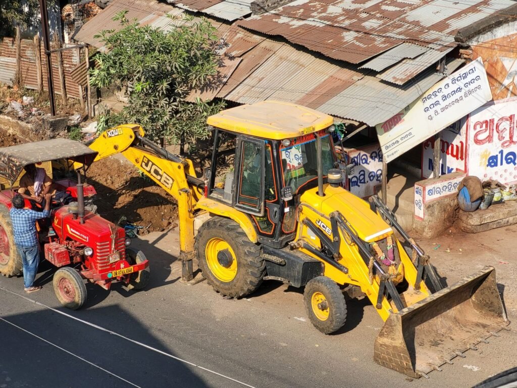 Retroexcavadora trabajando a un lado de un camino con el cargador frontal abajo