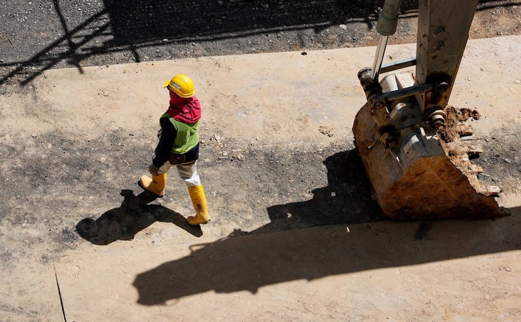 Trabajador con casco caminando cerca del cucharón de una excavadora en obra